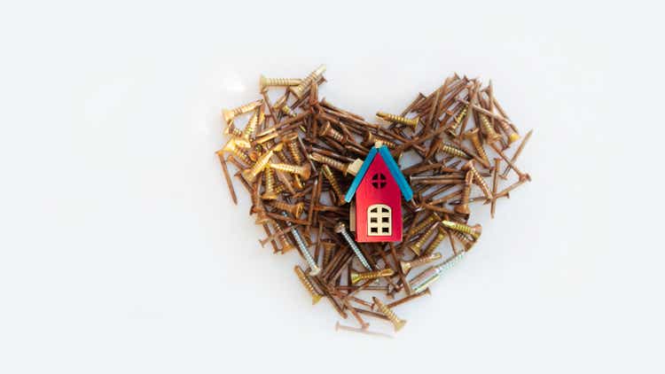 Pink wooden house model rests on piles of rusted nails. Heart shape. Homebuilding and repairing concept.