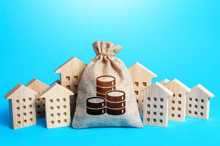 Money bag among town houses figurines. Municipal budgeting. Rich city. Rental business. Realtor services. Sale of real estate. property taxes. Tax collection, investment in city development.