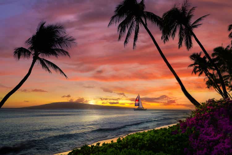 Puesta de sol hawaiana con velero y montañas
