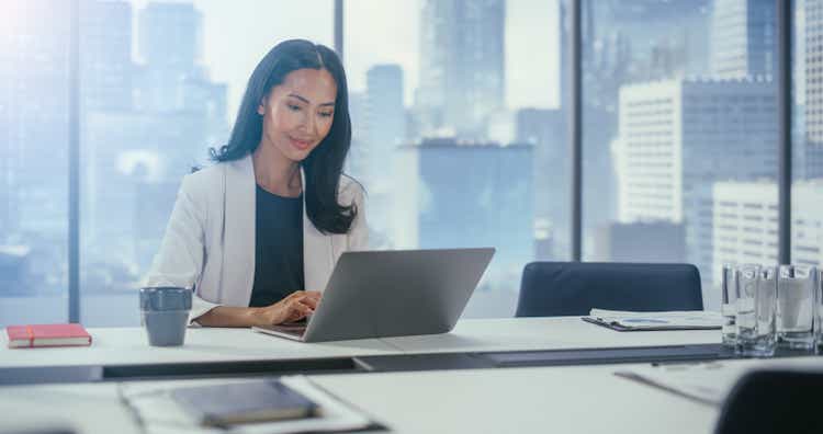 Portrait of Successful Asian Businesswoman Wearing in Stylish Suit Working on Laptop Computer in Big City Office. Powerful CEO Managing Digital e-Commerce Project, Data Analysis, Product Marketing