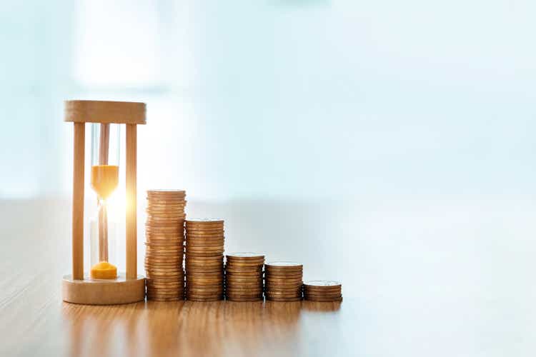 Hourglass and coins on wooden table