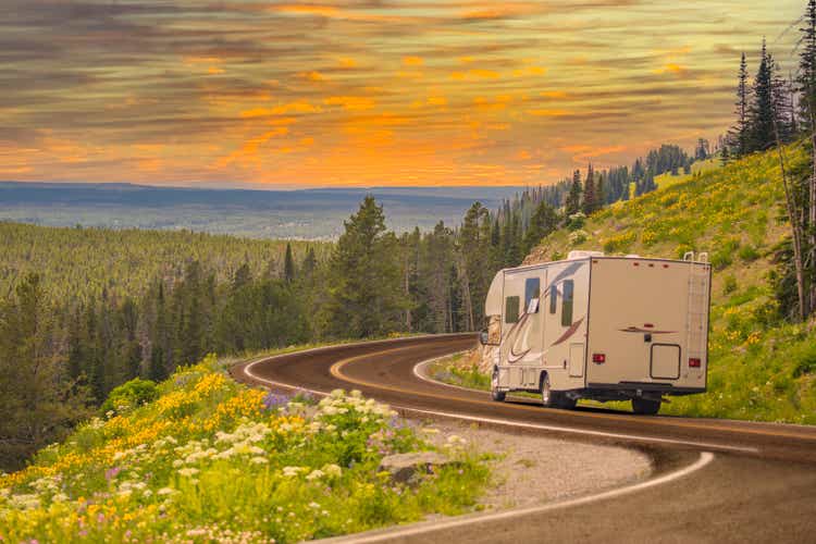 Camper Driving Down Road in The Beautiful Countryside Among Pine Trees and Flowers.