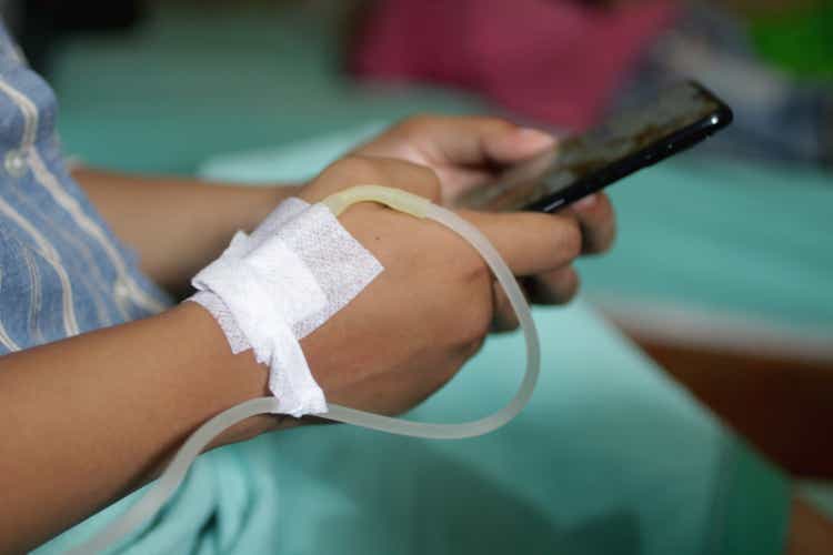 Female patient using phone with iv on hand in the hospital.