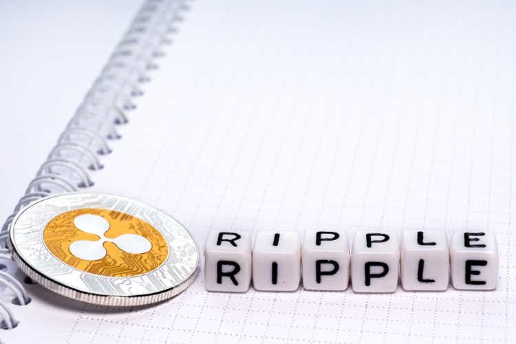 Crypto Coin XRP and word of cubes Ripple on paper sheet of opened spiral spring notebook.