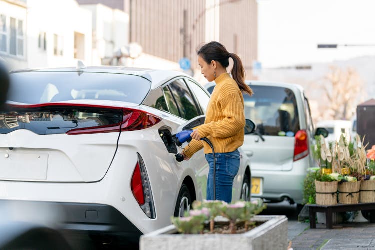 Mid adult woman plugging in an electric car to charge