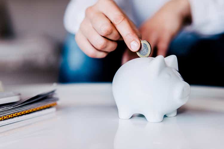 Putting a coin in a white piggy bank at home.