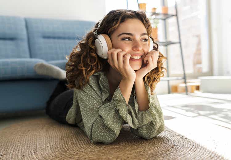 pretty curly-haired woman lying on the floor at home listening to music happy smiling relaxed