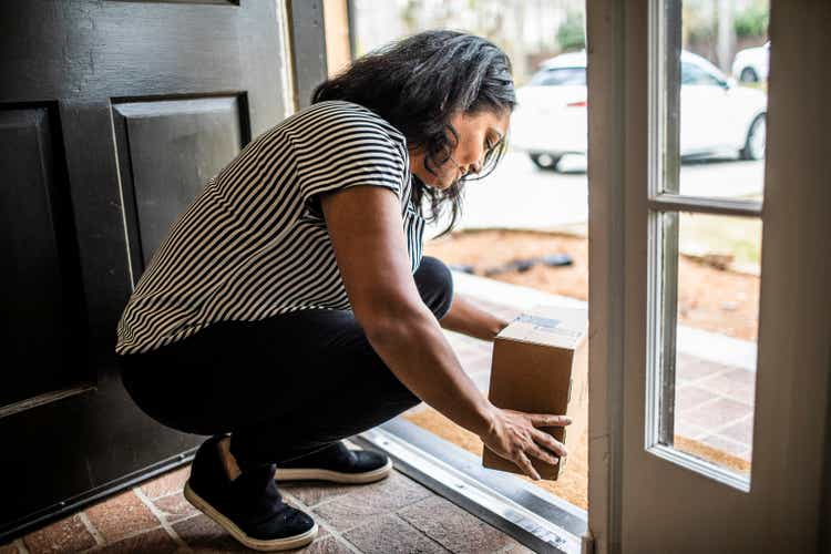 A woman collects a package for delivery at the door of the house
