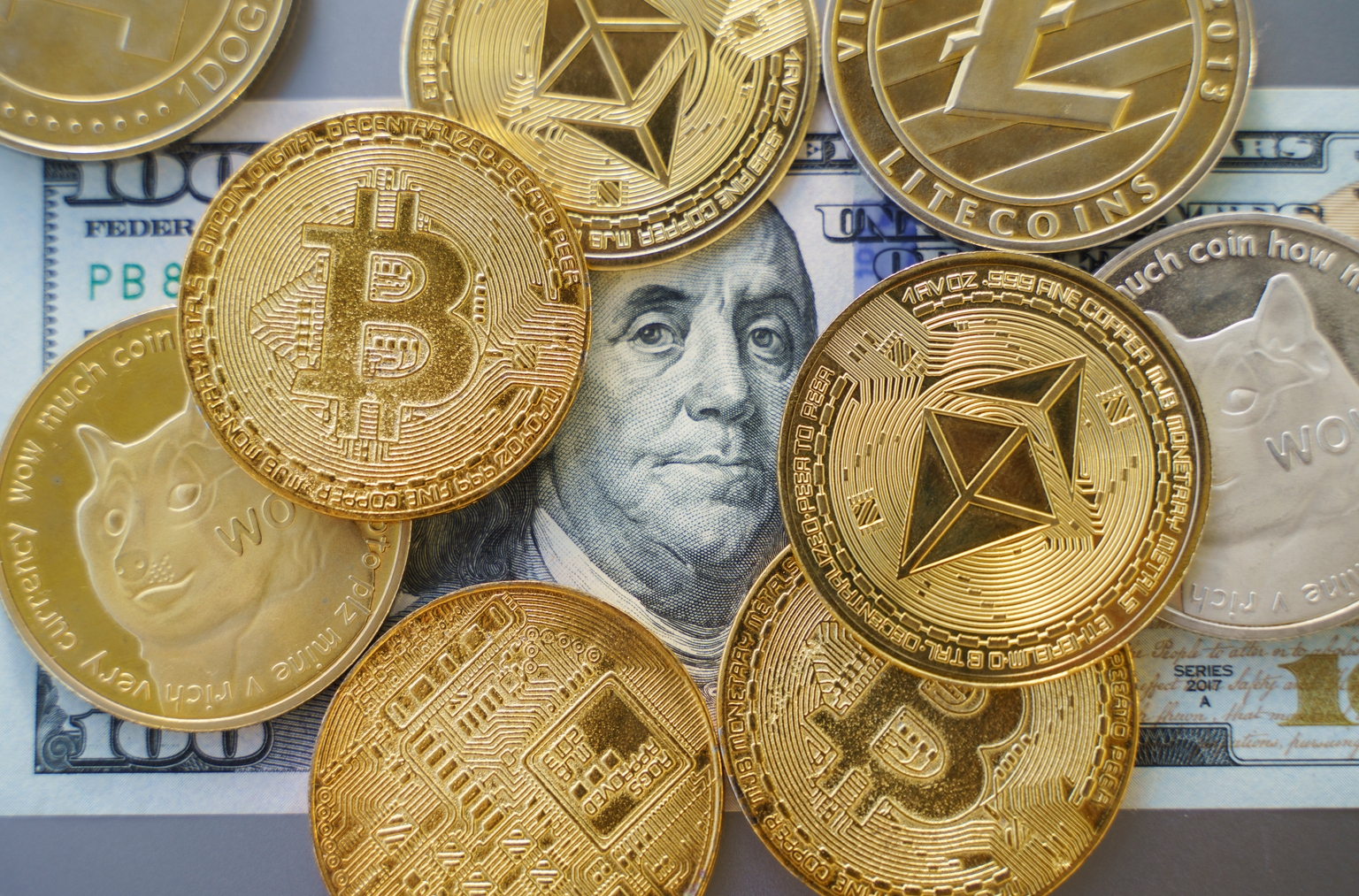 Close up shot of Bitcoin and alt coins cryptocurrency standing over a Hundred Dollar Bill. High angle view, no people