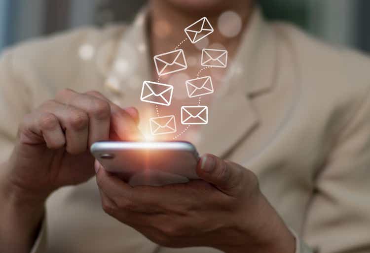 The notion of email. Close-up of a businesswoman typing on her phone, with email symbols on the virtual screen