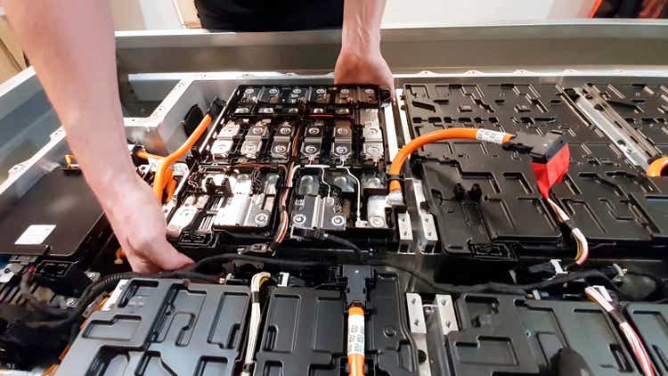 close-up of a mechanic"s hands disassembling an electric car battery on top of a trailer inside a mechanic shop