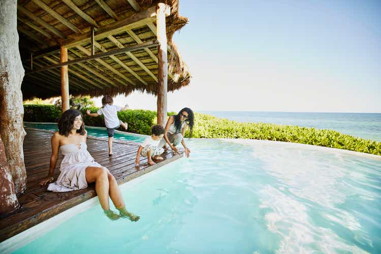 Wide shot of smiling mothers hanging out with sons by pool at luxury hotel suite