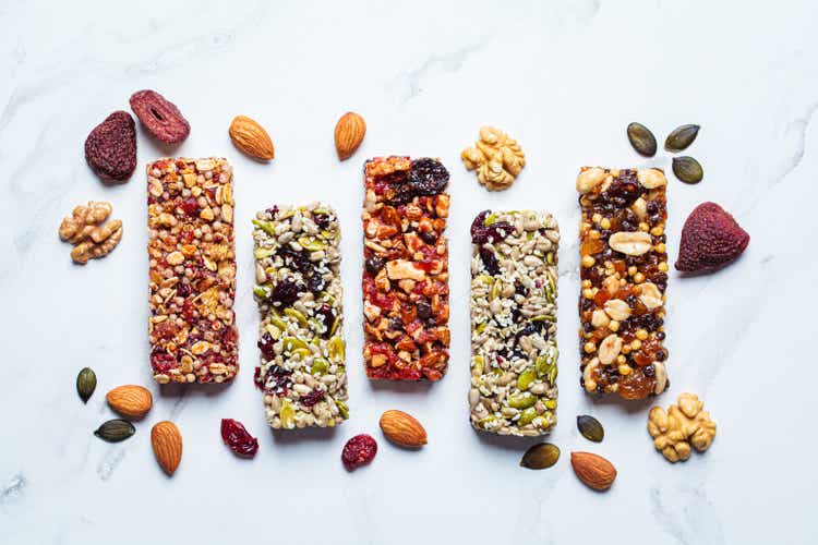 Energy granola bars with different seeds, nuts and dried fruits and berries on white marble background. Healthy snack concept.