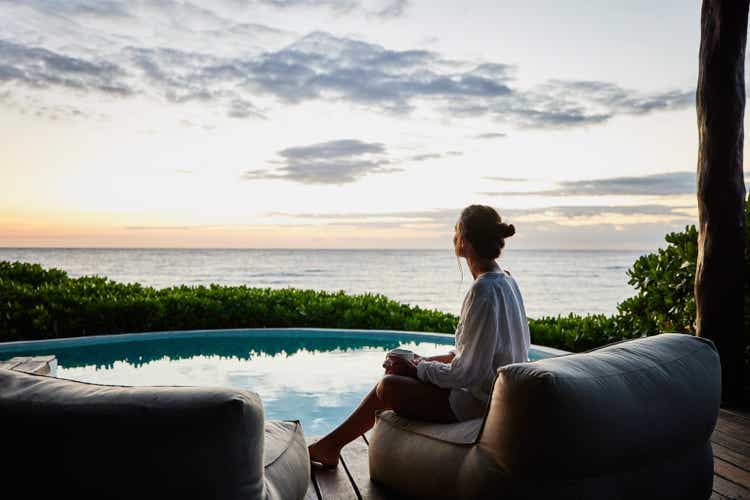 Wide shot of woman watching sunrise while sitting poolside at luxury suite at tropical resort