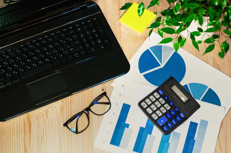 office workstation with laptop, calculator and graphs on a wooden countertop