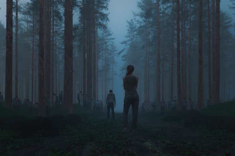 Woman standing in the spooky forest with hordes of zombies