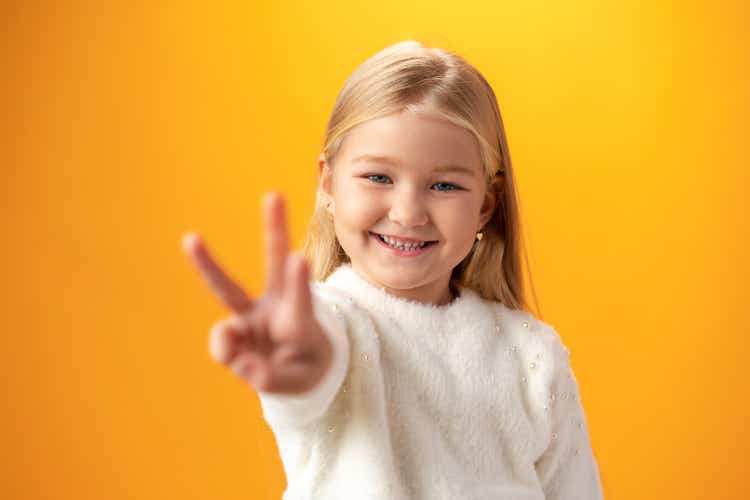 Little girl showing and pointing up with fingers number three against yellow background