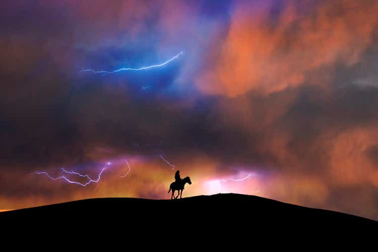 Silhouette of a lone rider on a horse standing on hill. Behind him is Dramatic storm sky and lighting behinde him the on the sky.