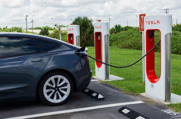 Grey Tesla Model Y electric car at Tesla Supercharger charging station.