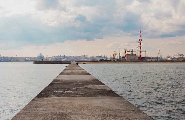 Chornomorsk, Ukraine - 04 20 21: Sea port. Cranes, boats and other industrial constructions, pier road going into perspective. Dramatic evening sky