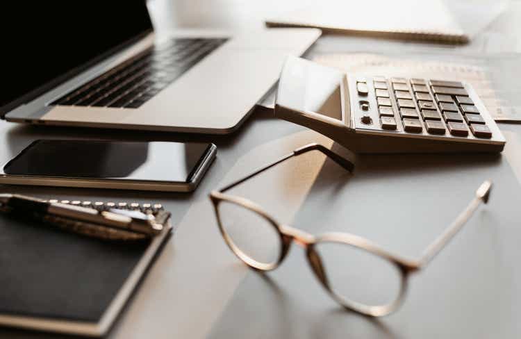 Place of work in office, calculator, laptop computer, glasses at office desk