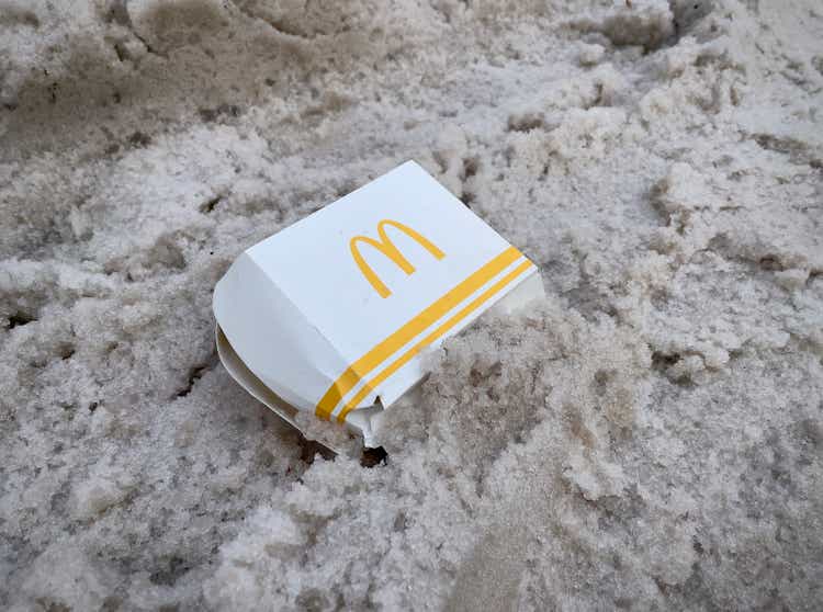 McDonald’s food packaging in dirty snow on the road. Fast food, MacDonald’s burgers. Disposable hamburger container. Dumped hamburger box. Environment issues.