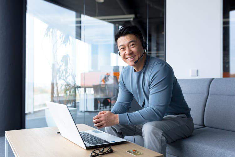 portrait of happy asian call center worker, man smiling and happy working with headset and computer, remote work, video call, online help