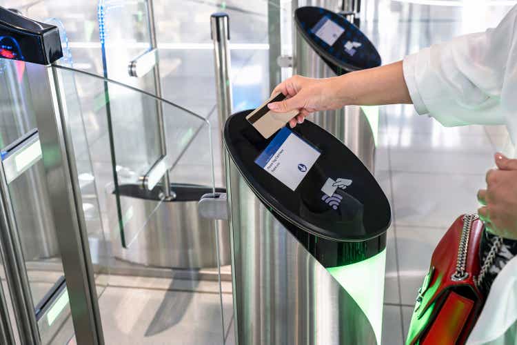 Woman"s hand applies a transport card to pass through the turnstile.