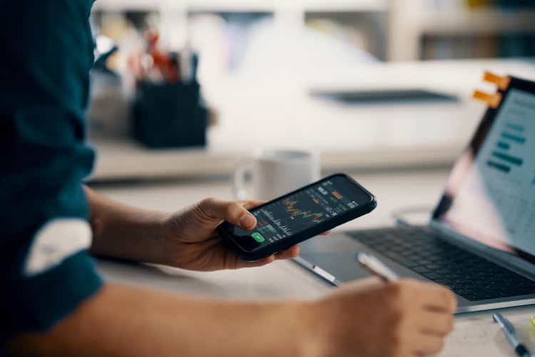 Mid adult man checking financial information on a smart phone while doing his bookkeeping