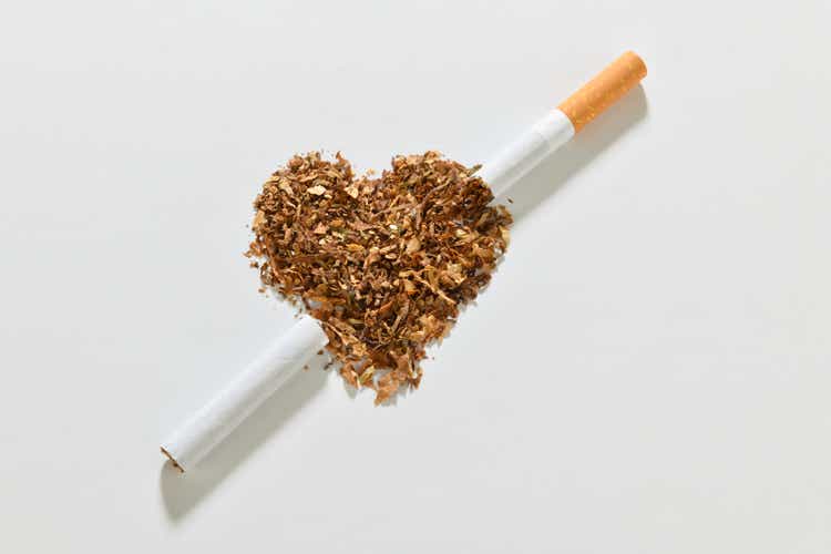 Broken cigarette over heart shaped tobacco isolated on white background.