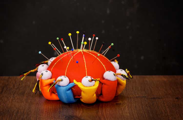 Red pincushion with colorful pins on wooden table and dark background
