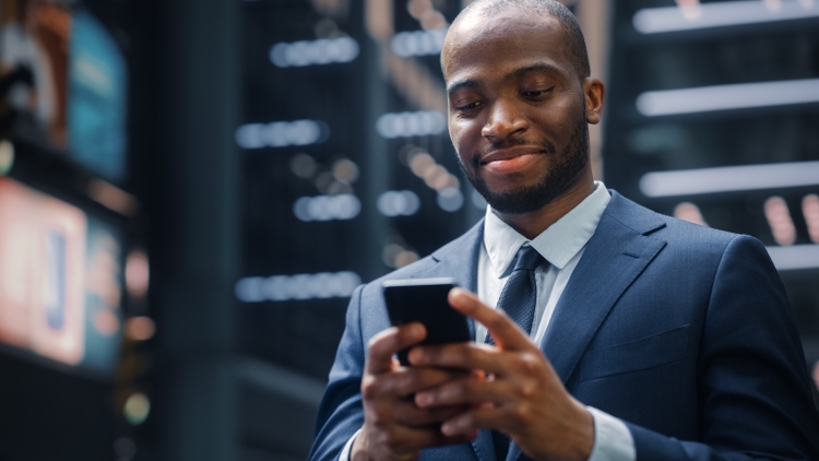 Portrait of Successful African-American Businessman on the Street of the Central Business District in Big City. Black Digital Entrepreneur uses Mobile Phone e-Commerce App for Stock Market Investment