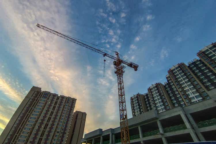A crane working on a construction site among residential buildings in suburb with background of sunset light.