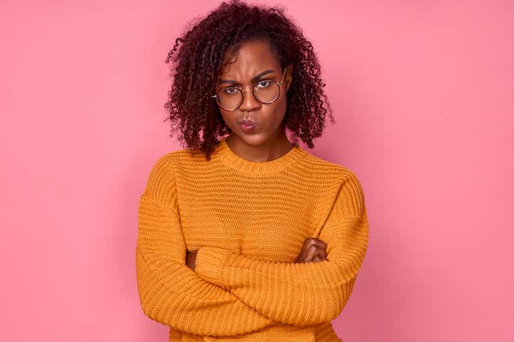 Sad young African American woman displeased looking at camera with crossed arms over pink background