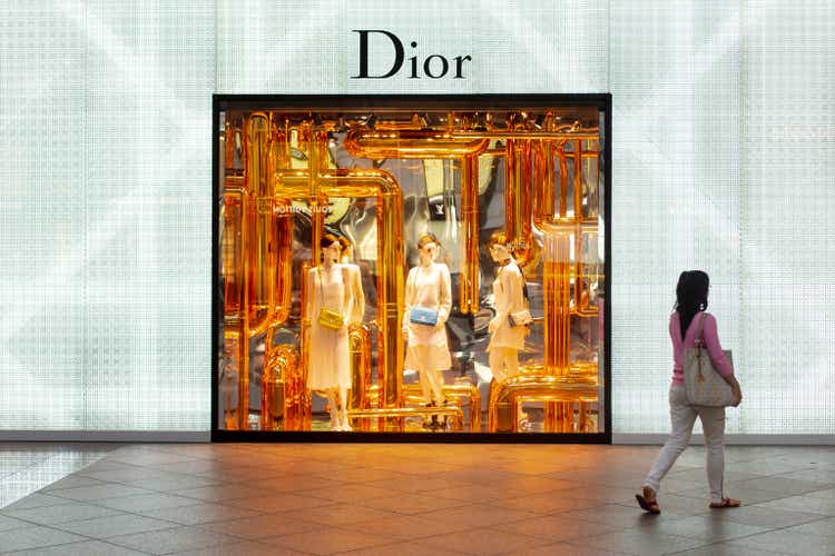 Woman shopping in front of the window of a Dior fashion boutique with the logo on the wall.