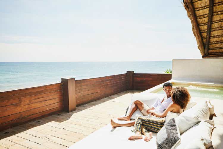 Wide shot of couple relaxing on deck of luxury tropical villa overlooking ocean