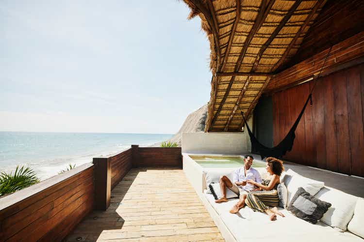 Wide shot of couple relaxing on deck of luxury tropical villa overlooking ocean