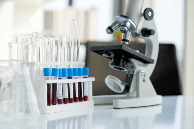 Blood collection tubes from covid 19 patients place next to microscope on white laboratory table. Coronavirus disease 2019 testing process in a laboratory preventing the spread of viral research.