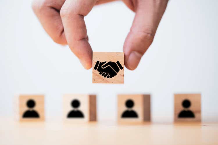 Hand holding wooden cube which drawing of hand shaking print screen on wooden cube block in front of human icon for business deal and agreement concept.