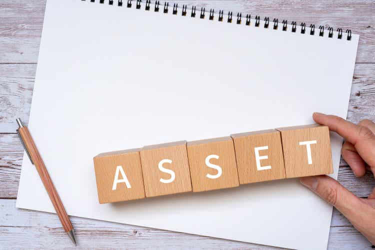 Wooden blocks with "ASSET" text of concept, a pen, a notebook, and a hand.