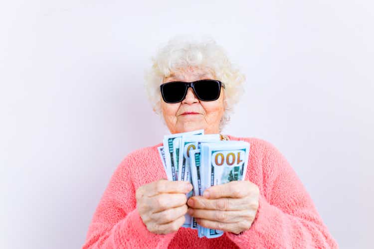 blonde old lady wear pinl sweater and sunglasses showing money isolated white background