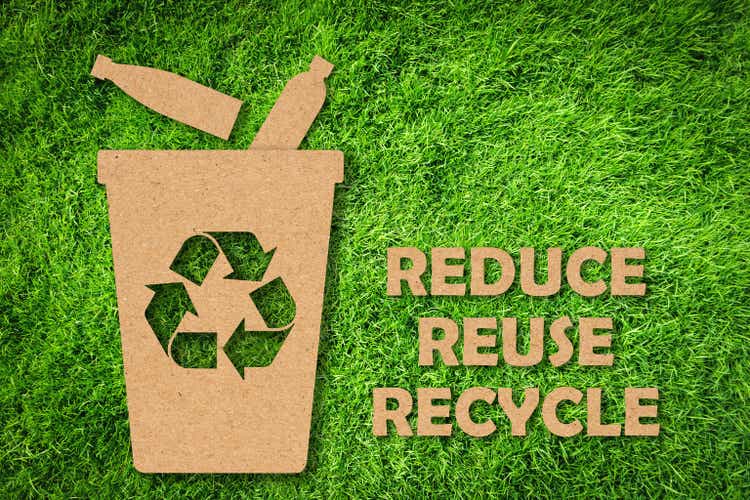 Kraft paper cut of Reuse, Reduce, Recycle symbol and text on green grass background. Environmental conservation concept.