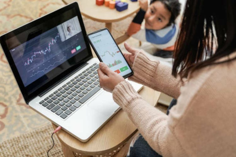 Trader mother studying stock market on streaming lesson with her child at home - Blockchain analysis concept - Focus on left hand holding mobile phone