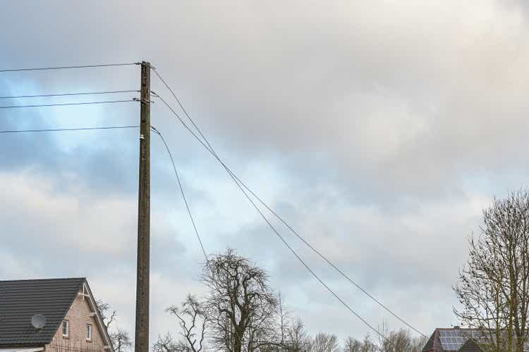 Concrete power pole with torn overhead transmission lines, storm damage in a rural village, cloudy sky with copy space