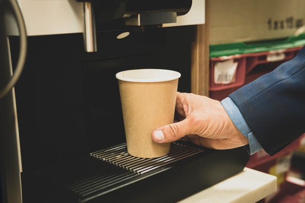 cropped view of businessman pushing button on coffeemaker while preparing coffee to go. man takes coffee from a vending machine