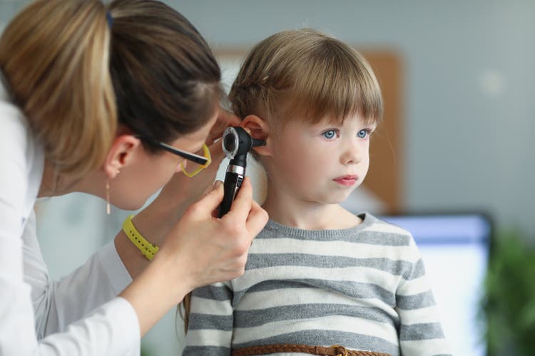 Female pediatrician looking at ear of little girl using otoscope in clinic