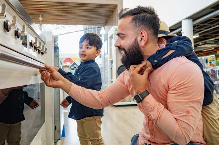 A father and two sons looking at ovens in an appliance store.