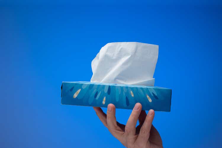 Paper tissue dispenser held by Caucasian male hand. Close up studio shot, isolated on blue background