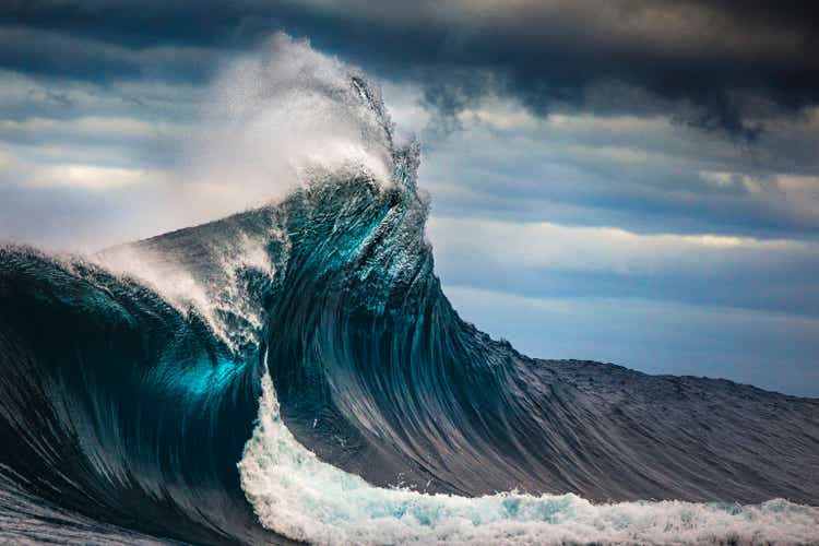 Tall powerful cross ocean wave breaking during a dark, stormy evening.