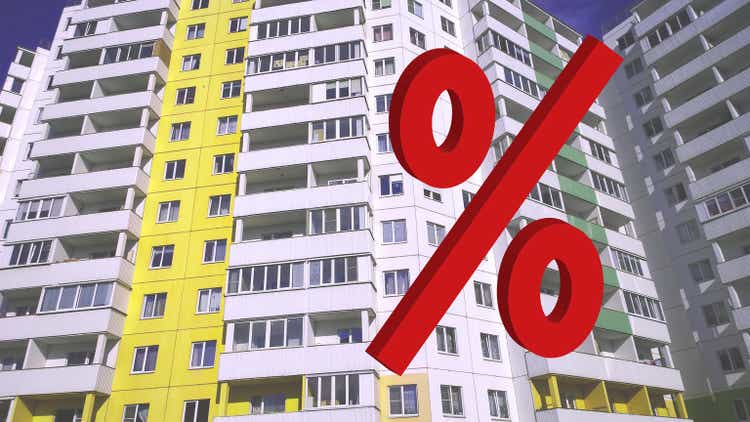 Red Percentage sign on facade background of new residential building. Interest rates. House Share. Real estate investing. Buy, sale, rental and insurance apartment in crisis. Mortgage. Forecasting.